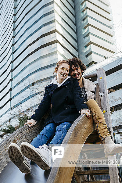 Portrait of happy couple on a slide at a playground in the city