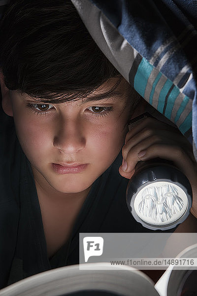 Junge liest mit Taschenlampe unter einer Decke