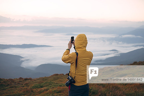 Mann in gelber Jacke beim Fotografieren mit dem Smartphone in den Karpaten