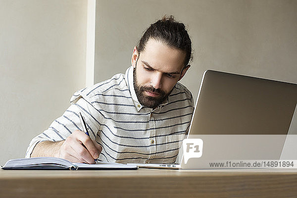 Young businessman with laptop writing in note pad