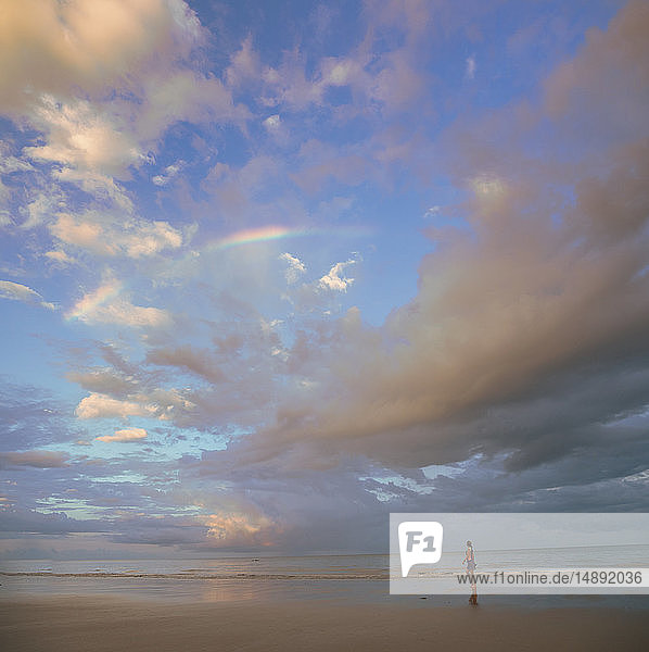 Wolkenlandschaft über einer am Strand spazierenden Frau in Port Douglas  Australien