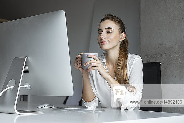 Junge Geschäftsfrau hält Kaffeetasse am Schreibtisch