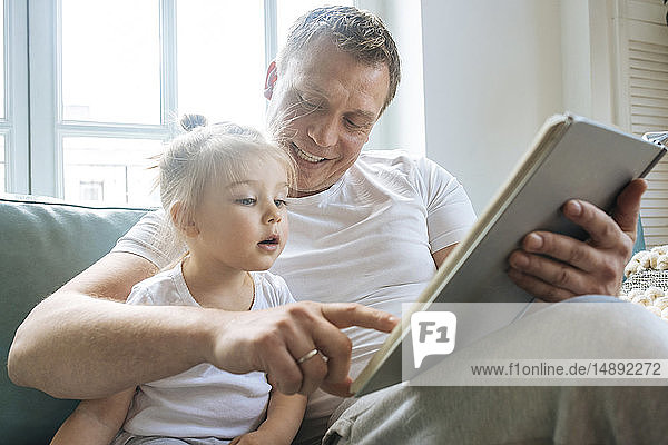 Father reading book to daughter on sofa