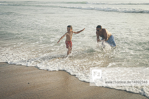 Vater bespritzt Sohn am Strand