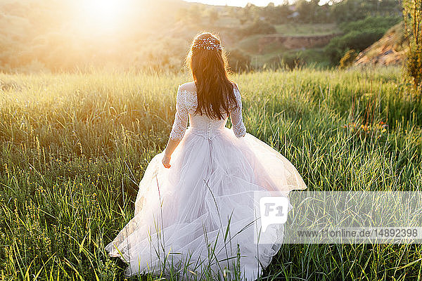 Rückansicht der Braut im Hochzeitskleid  die im Gras läuft
