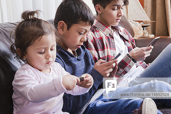 Siblings using smart phones on sofa