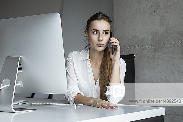 Junge Geschäftsfrau  die am Schreibtisch telefoniert