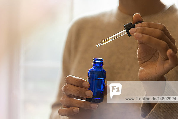 Frauenhand hält Pipette und Flasche mit Aromatherapieöl