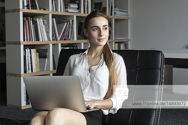 Junge Geschäftsfrau arbeitet mit Laptop auf dem Sofa