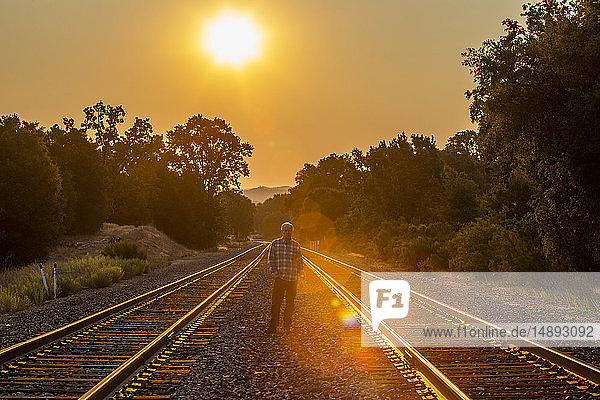 Älterer Mann steht bei Sonnenuntergang zwischen Eisenbahnschienen