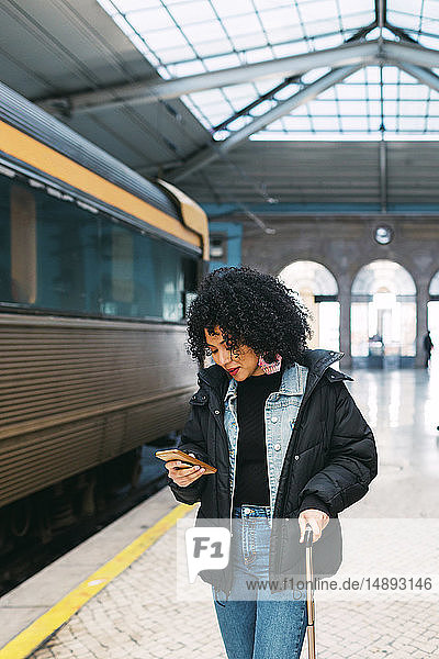 Junge Frau benutzt Smartphone im Bahnhof