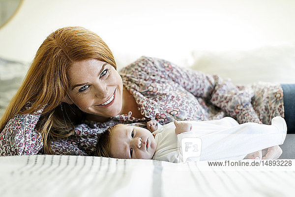 Lächelnde Frau mit ihrem neugeborenen Sohn auf einem Bett liegend