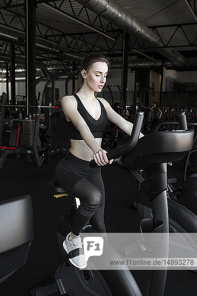 Young woman using exercise bike in gym