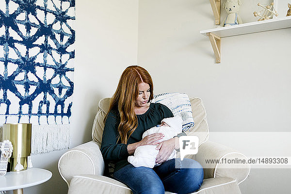Frau hält ihren neugeborenen Sohn auf einem Sessel