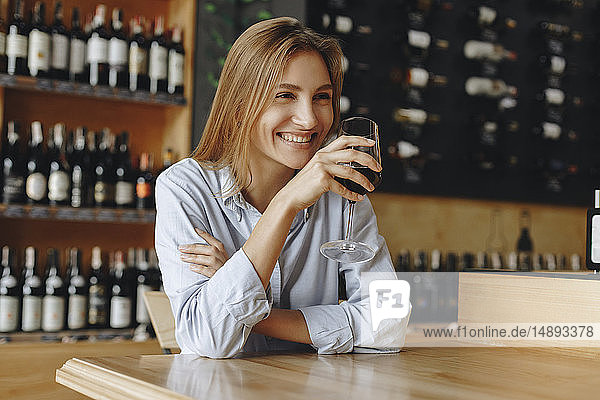 Lächelnde junge Frau hält ein Glas Rotwein