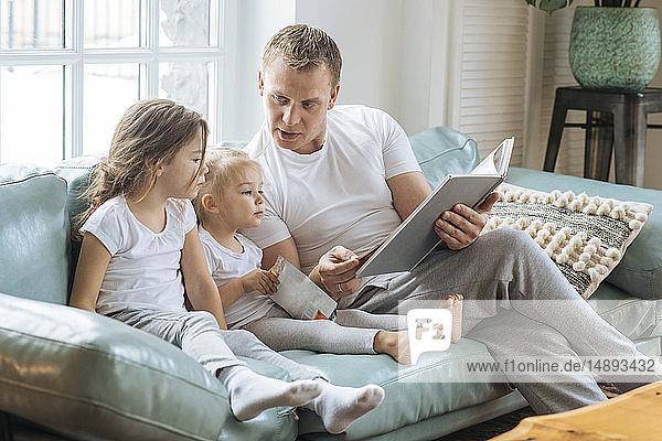 Vater liest Töchtern auf dem Sofa ein Buch vor