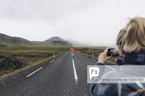 Junge Frau fotografiert ihren Freund beim Gehen auf der Landstraße in Island