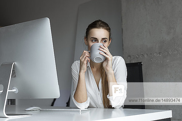 Junge Geschäftsfrau trinkt Kaffee am Schreibtisch