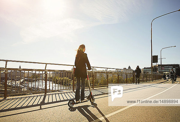 Frau in voller Länge auf Elektroschubroller auf Brücke gegen blauen Himmel