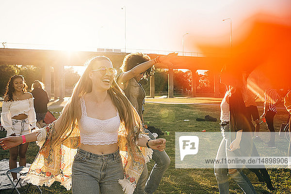 Fröhliche junge Frau tanzt mit Freunden an einem sonnigen Tag bei einer Musikveranstaltung