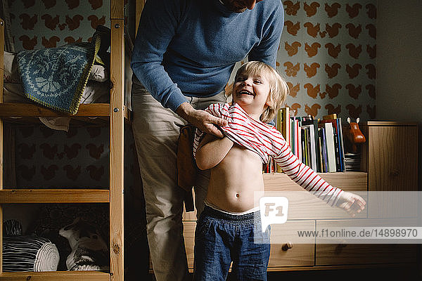 Father dressing cheerful daughter at home