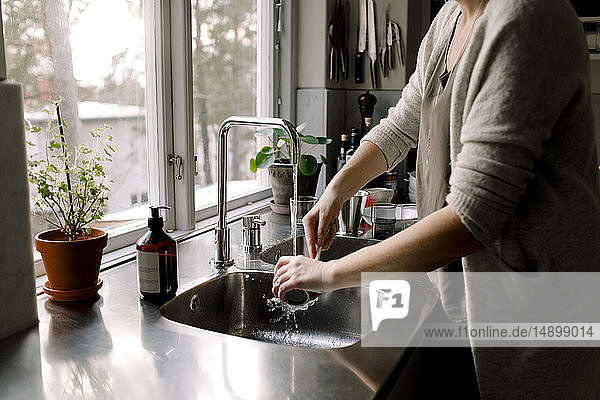Mittelteil einer Frau  die eine Tasse in der Küchenspüle zu Hause putzt