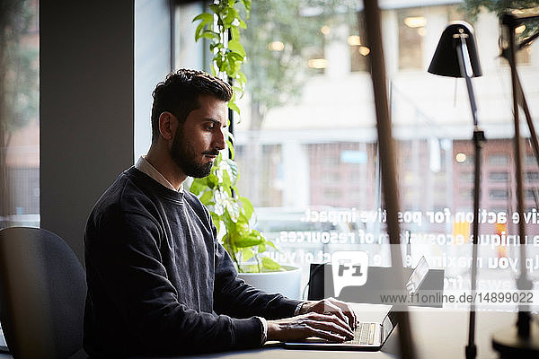 Kreativer Geschäftsmann mit Laptop am Schreibtisch im Kreativbüro