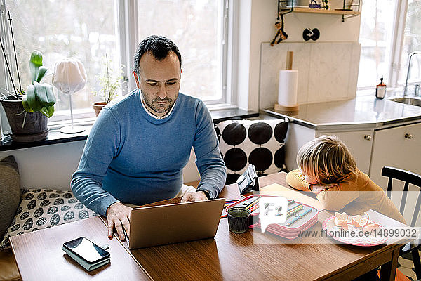 Ernsthafter Vater benutzt Laptop  während die Tochter zu Hause ein Handy benutzt