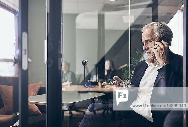 Ein reifer männlicher Manager telefoniert mit dem Handy durch eine Glaswand im Kreativbüro