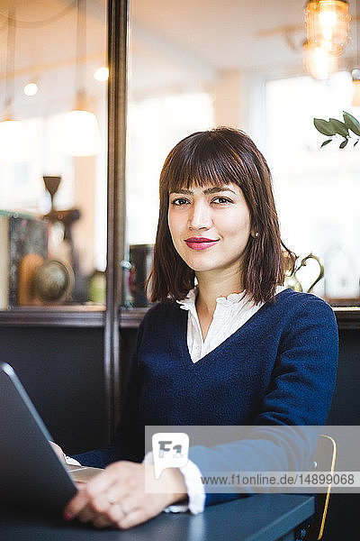 Portrait of confident female professional sitting with laptop at office