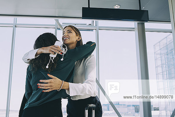 Niedriger Blickwinkel einer lächelnden Geschäftsfrau  die einen Kollegen im Korridor des Flughafens umarmt
