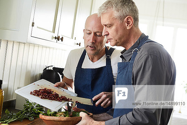 Bald mature man assisting friend in cooking food at home