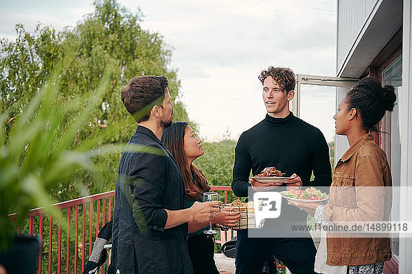 Young man talking with friends while holding meal during party on terrace