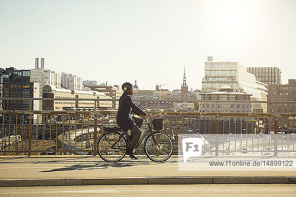 Ganzflächige Seitenansicht eines jungen Mannes auf einem Elektrofahrrad auf einer Brücke in der Stadt