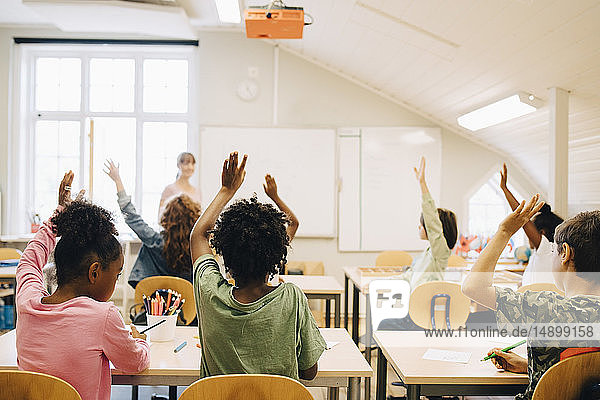 Students raising hands while answering in classroom at school