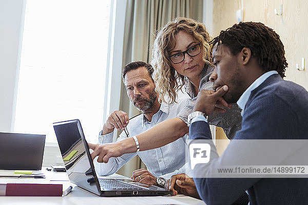 Seriöse reife Geschäftsfrau schaut einen männlichen Kollegen an  während sie im Sitzungssaal einen Laptop benutzt