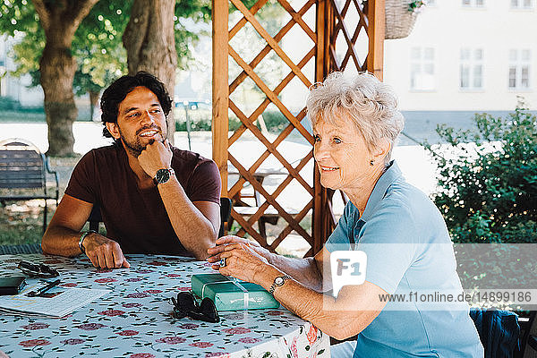 Lächelnder männlicher Hausmeister schaut auf ältere Frau  die mit einem Geschenk im Hinterhof sitzt