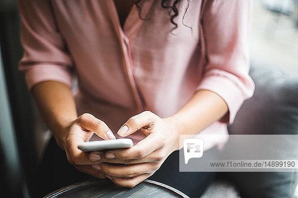 Mittendrin junge Geschäftsfrau mit Textnachrichten vom Smartphone im Kreativbüro