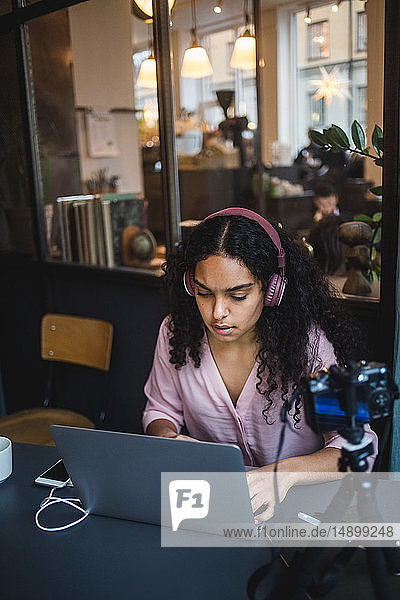 Selbstbewusste junge Einflussnehmerin benutzt Laptop  während sie am Schreibtisch im Kreativbüro vloggt
