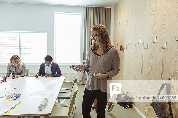 Lächelnde Geschäftsfrau liest Dokument  während Kollegen im Hintergrund am Konferenztisch arbeiten