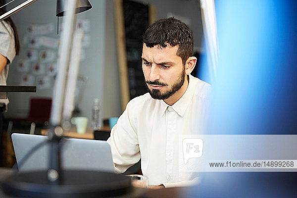 Stressed businessman looking at laptop while sitting in creative office