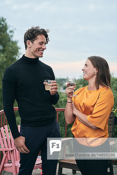 Fröhliche Freunde unterhalten sich  während sie während der Party auf der Terrasse Getränke halten