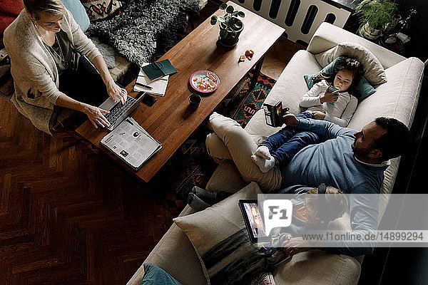 Hochwinkelansicht der Familie unter Verwendung verschiedener Technologien im Wohnzimmer zu Hause
