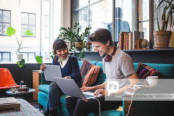 Smiling multi-ethnic male and female professionals discussing over laptop on sofa at office