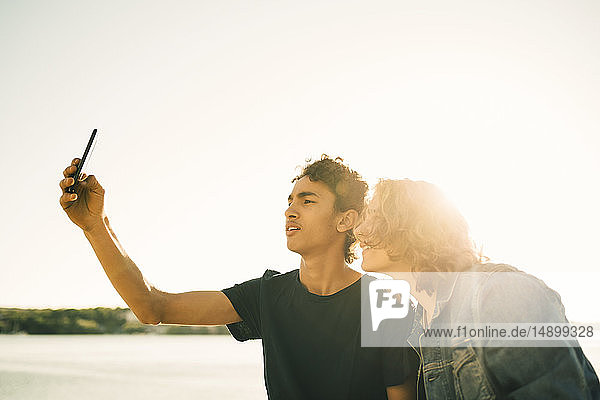 Freunde nehmen Selfie mit dem Handy gegen den klaren Himmel in der Stadt bei Sonnenschein