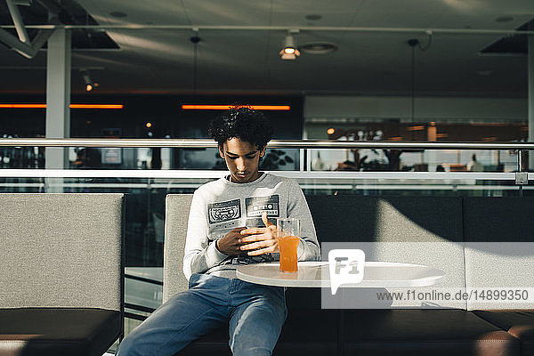 Teenager-Junge benutzt Mobiltelefon  während er im Restaurant sitzt