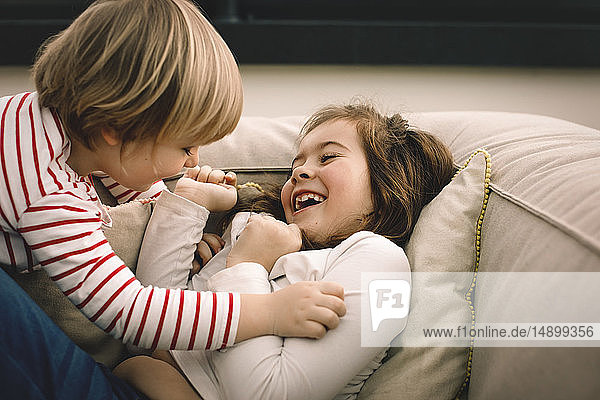 Verspieltes Mädchen kitzelt fröhliche Schwester zu Hause auf der Couch