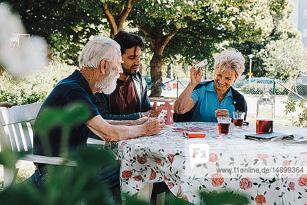 Fröhliche ältere Frau spielt mit Männern am Tisch im Hinterhof Karten