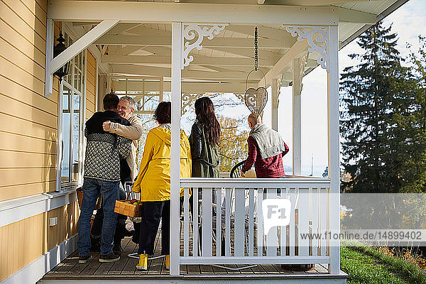 Happy mature men embracing while standing on porch by friends