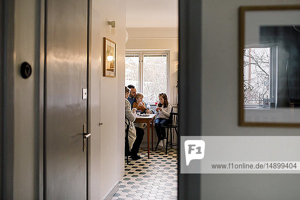 Family sitting on chairs in kitchen seen through doorway at home